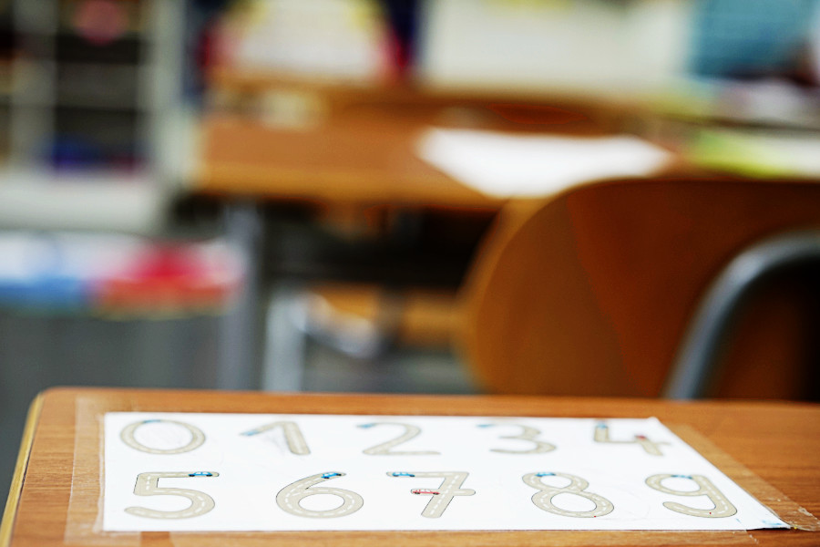 Tisch in einem Klassenzimmer. Auf dem Tisch liegt ein Blatt mit den Zahlen Null bis Neun.